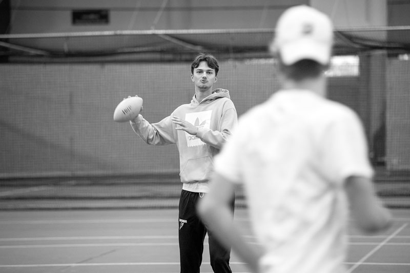 A person in a hoodie holds a football, practicing physical education with another in a cap.
