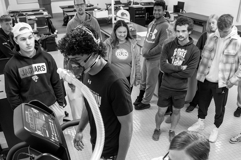 A group observes exercise science testing as a person on a treadmill wears a breathing mask.