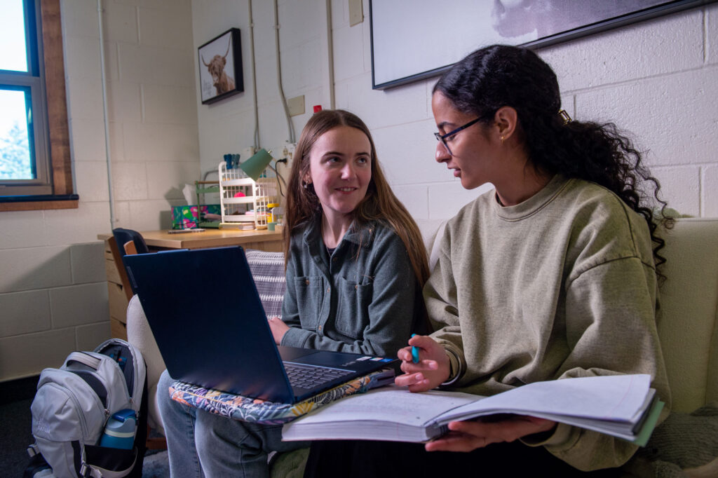 Two women sit on a couch studying together, enjoying a moment of residence life.