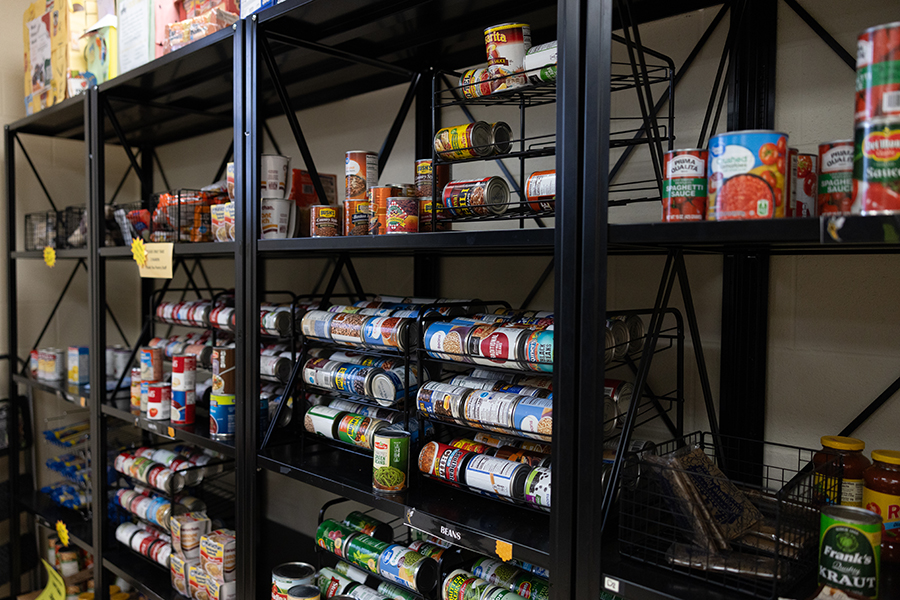 Shelves stocked with various canned foods and non-perishable items, organized in rows. The scene appears to be in a food pantry or storage room with black metal shelving.