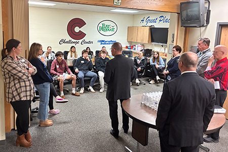 A group of people sit and stand in a classroom while one person speaks to the group.