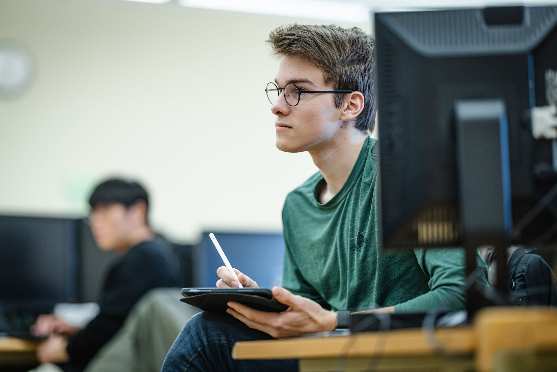 A person in glasses studies Computer Science Education with a stylus on a tablet at their desk.