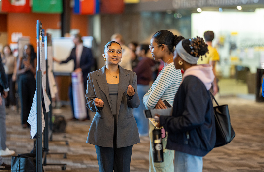 Person in a suit presents a SURF poster to two people in the Yellowjacket Union.