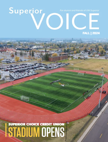 Aerial view of a stadium with a green soccer field, red running track, and people gathered at the center. Cars fill the parking lot. Text reads “Superior VOICE, Fall 2024. Celebrating Alumni Achievements as Stadium Opens.”.