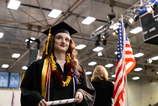A graduate with an academic microcredential holds a diploma near an American flag.