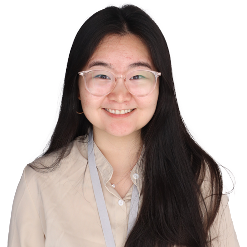 A young woman with long black hair and clear glasses smiles at the camera, embodying confidence and superior outcomes. She is wearing a beige blouse and a gray lanyard with a badge against a plain white background.